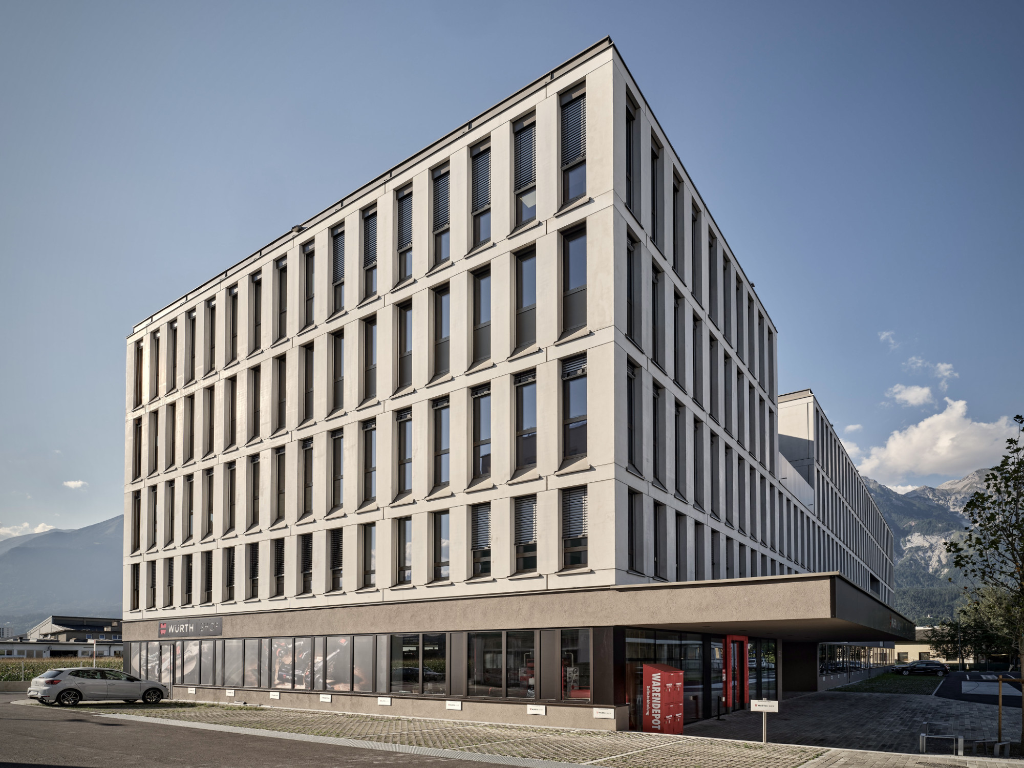 Helga Krismer Platz, Innsbruck, Gebäudeecke mit vertikal gegliederter Betonfassade und Erdgeschoss-Ladenzone