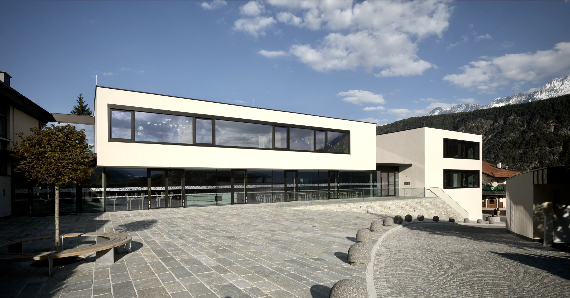 Kindergarten Rietz, Fassadenansicht mit auskragendem Obergeschoss über verglastem Erdgeschoss und Steinplatz