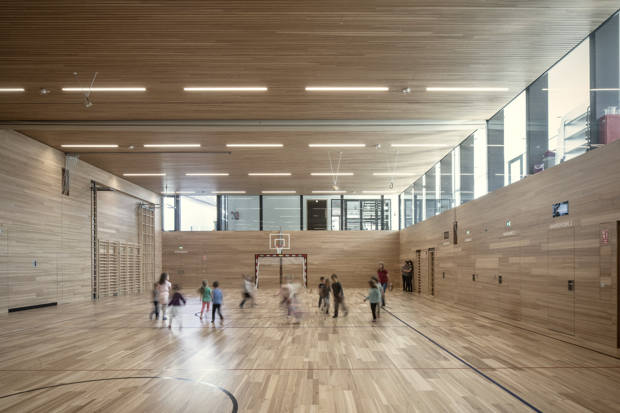 Kindergarten Rietz, Turnsaal mit Eichenparkett und Wandvertäfelung aus Holz beim Kinderspiel
