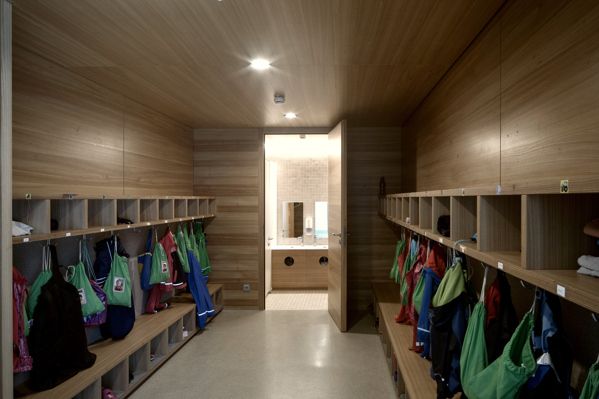 Kindergarten Rietz, Garderobe mit Holzfächern, Kleiderhaken und Blick auf gefliestes Waschbecken