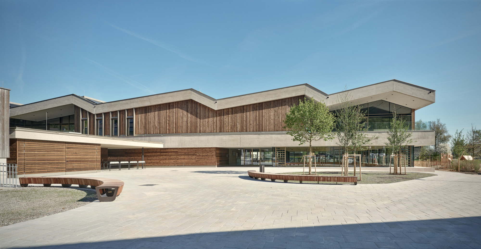 Volksschule Fürstenbrunn, Gebäudeansicht mit Holzfassade, Sichtbeton und begrüntem Vorplatz